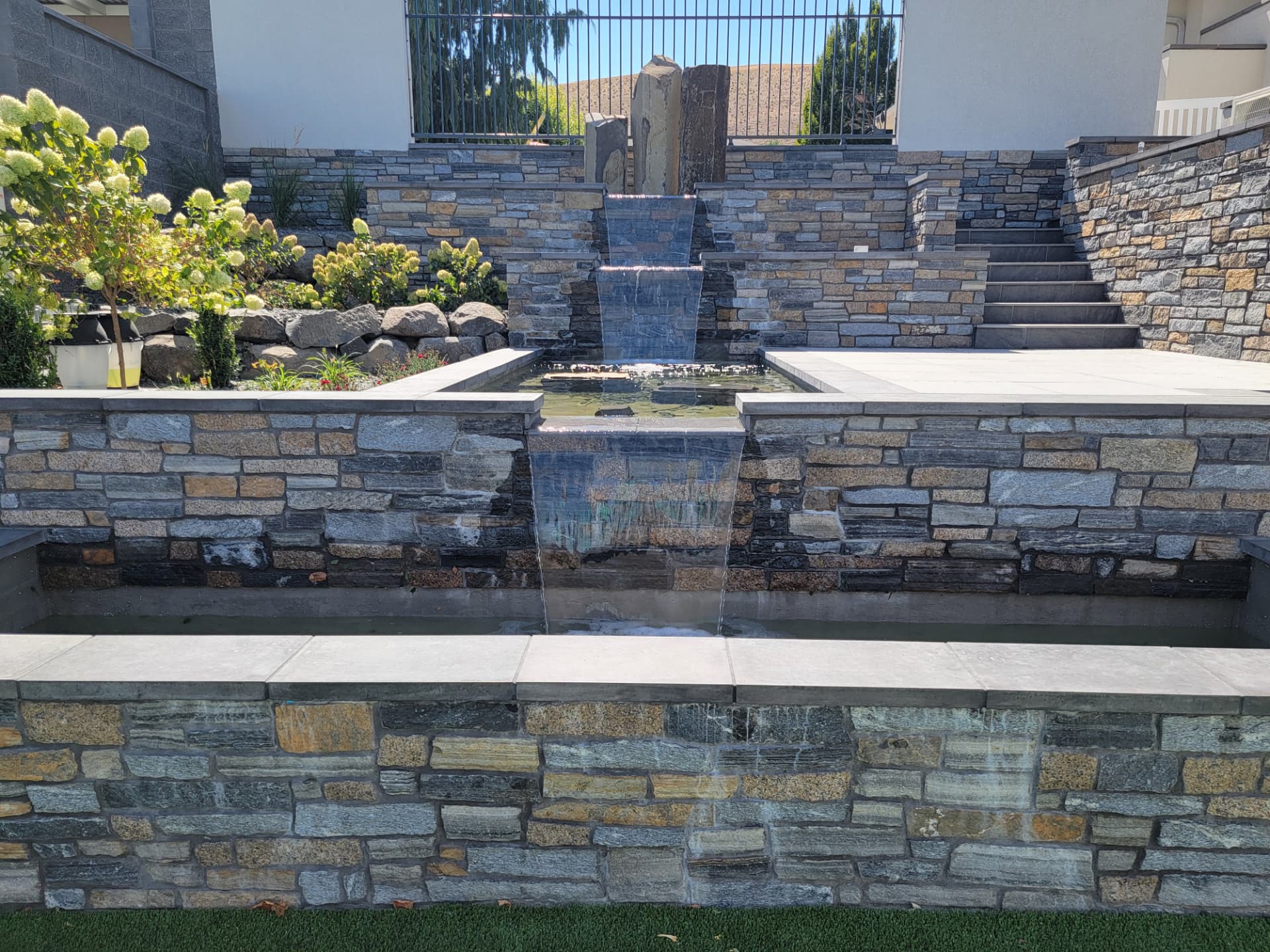 Tiered natural stone water feature with sheer waterfall spillways into a reflecting basin